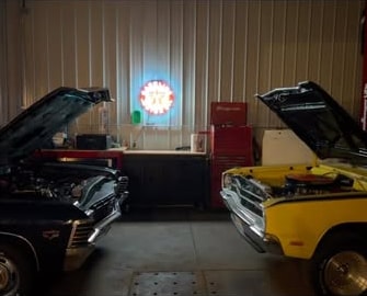 Two classic muscle cars sitting hood-up across the working bay at 2240 Speed Shop