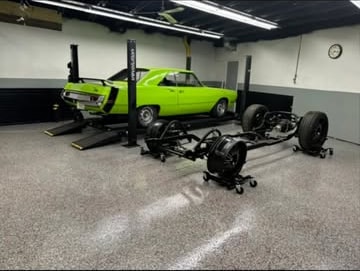 Bright green classic coupe beside a freshly assembled rolling chassis in the shop