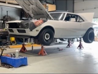 White classic coupe raised on stands during mechanical work at 2240 Speed Shop