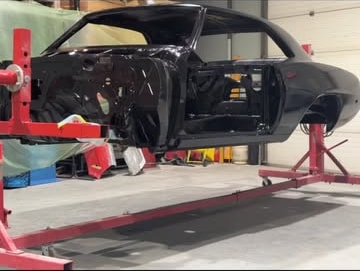 Black coupe shell secured to a rotisserie for restoration work