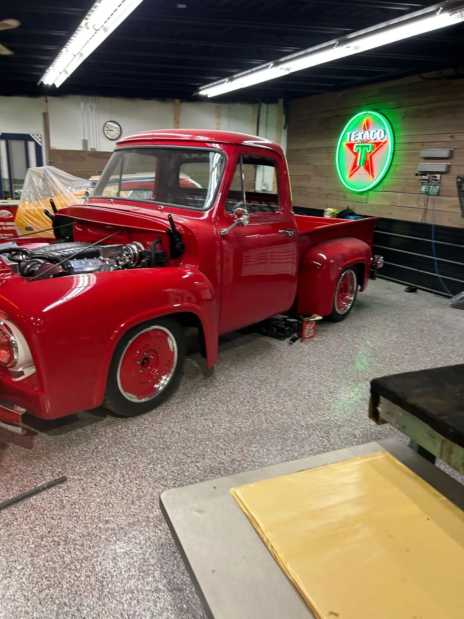 Red 1950s stepside pickup with the hood up beside the Texaco neon sign inside the 2240 Speed Shop bay in Edmonton